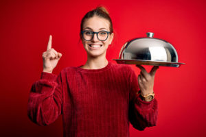 A smiling woman holding a covered food tray.