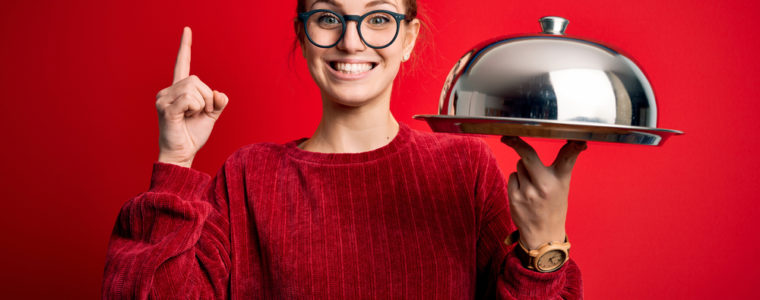 A smiling woman holding a covered food tray.