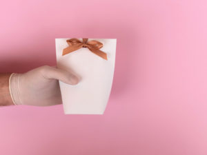 A gloved hand holding a small gift pouch with a bow on it.