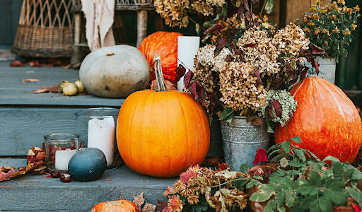 Pumpkins and Fall flowers decorate the entrance to a home.